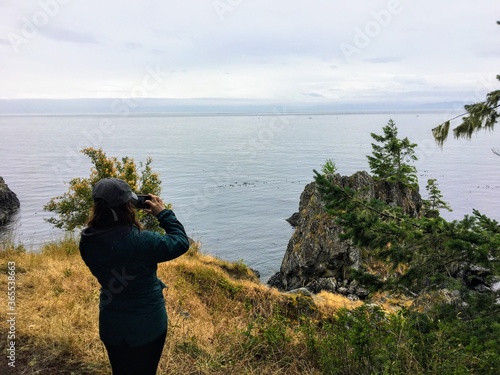 Wallpaper Mural A woman along the coast of Vancouver Island along the east sooke coast trail taking a photo overlooking the wide ocean of the Juan de Fuca straight in British Columbia, Canada. Torontodigital.ca
