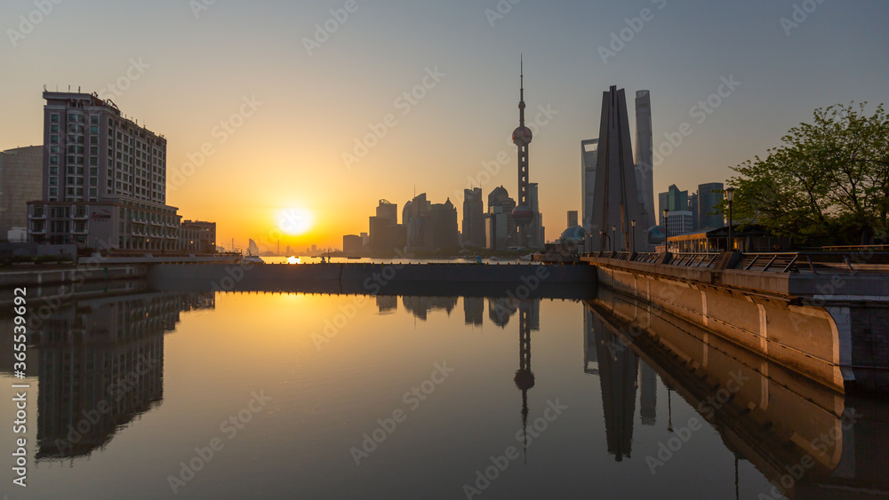 Dusk at Shanghai - panorama with sun rising over Pudong. Reflections of skyscrapers in the water.