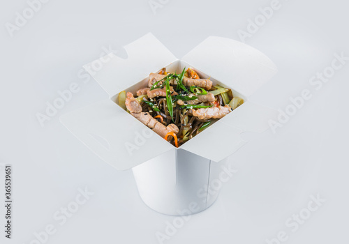 Isolated Asian Soba Buckwheat Noodles with pork meat fillet, vegetables, soy sauce and spring onion scallions in white carton takeaway delivery box. Food delivery package with ready to eat dish inside