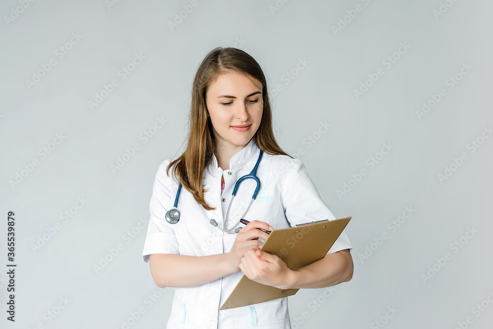 Young handsome woman over isolated grey background with doctor gown and writing in a folder Young handsome woman over isolated grey background with doctor gown and writing in a folder