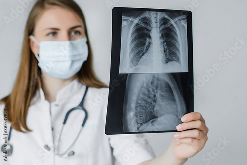 young beautiful doctor radiologist look learn waych human skeleton of lungs. A woman in a white coat with a mask and stethoscope on her neck is studying fluorography. Selective focus photo