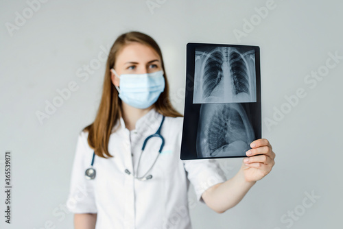 doctor radiologist look learn waych human skeleton of lungs. A woman in a white coat with a mask and stethoscope on her neck is studying fluorography. photo