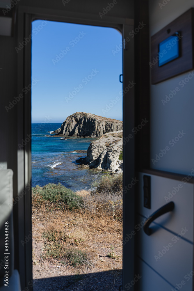 Fototapeta Views of a cliff and a beach with blue sea through the door of a parked motorhome van.