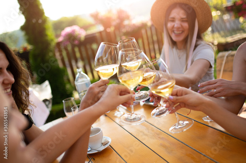 Young female friends clinking glasses with wine on the summer terrace of cafe or restaurant