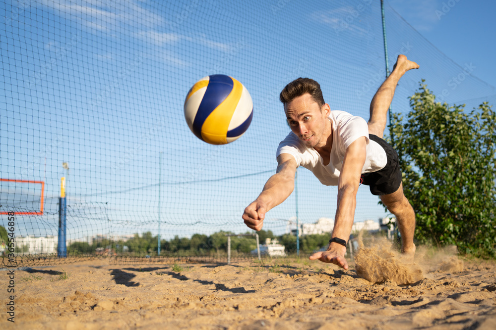 Playing volleyball on the beach, the guy hits the ball in a jump.