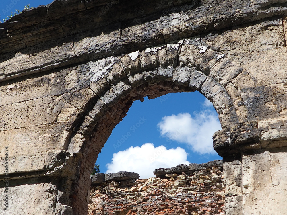 arched opening of a ruined ancient red brick building against a blue cloudy sky