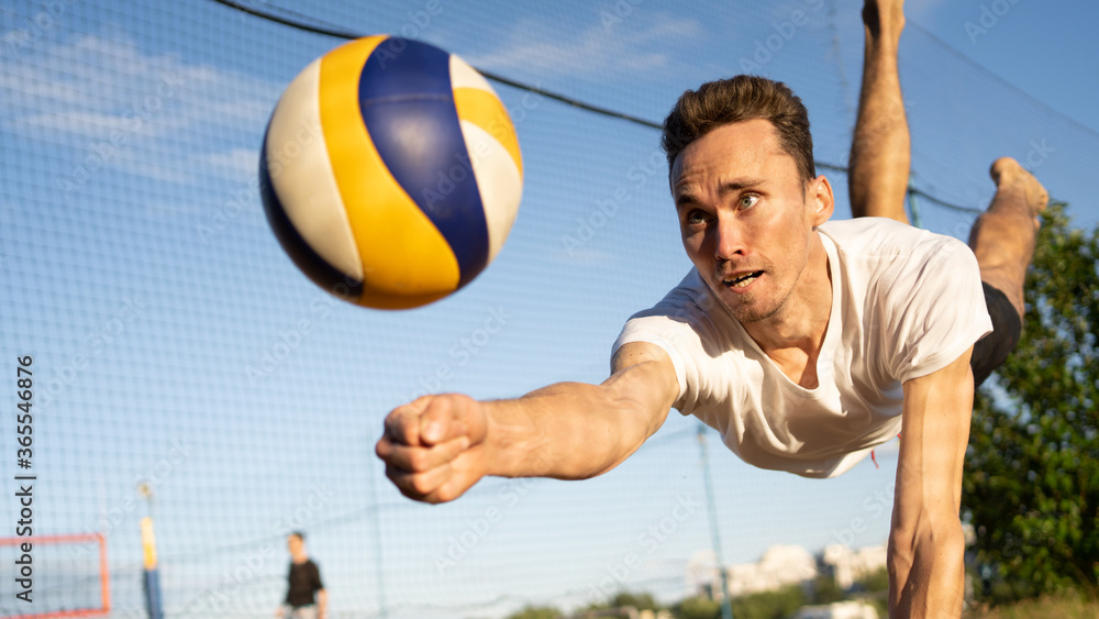 Playing volleyball, the guy hits the ball in a jump.
