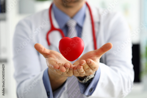 Male medicine doctor hands holding and covering red toy heart photo