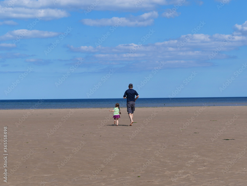 father and daughter running on the beach towards the sea