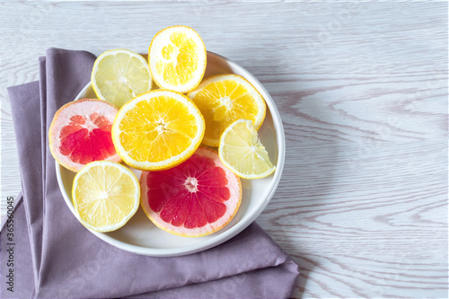 Citrus fresh orange grapefruit fruits on plate with napkin on wooden background with copy space