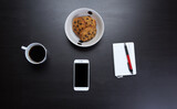 Modern smartphone with blank screen lying flat on coffee table beside some brownies, coffee cup and a notebook