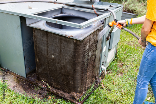Person cleaning dirty condenser coils on an air conditioner system