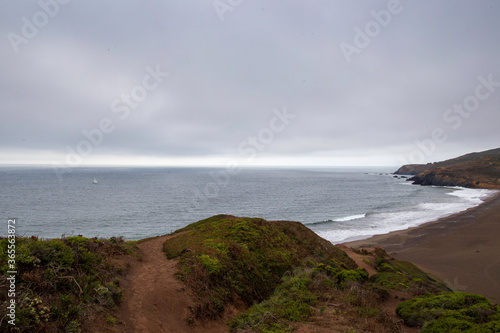 Deserted dunes and beach with lone sailboat in distance on grey overcast day photo