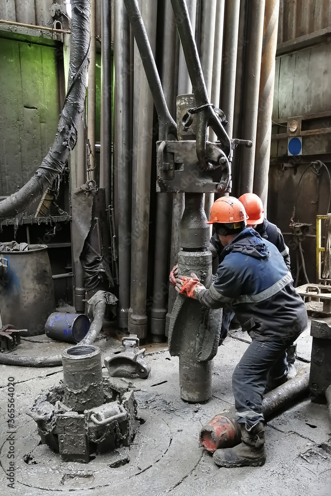 Two drilling crew workers dismantle the bottom of the drill string. Unscrewing the spiral calibrator. Working with a machine key. They are located on the rotary platform of the drilling rig. Two drilling crew workers dismantle the bottom of the drill string. Unscrewing the spiral calibrator. Working with a machine key. They are located on the rotary platform of the drilling rig.