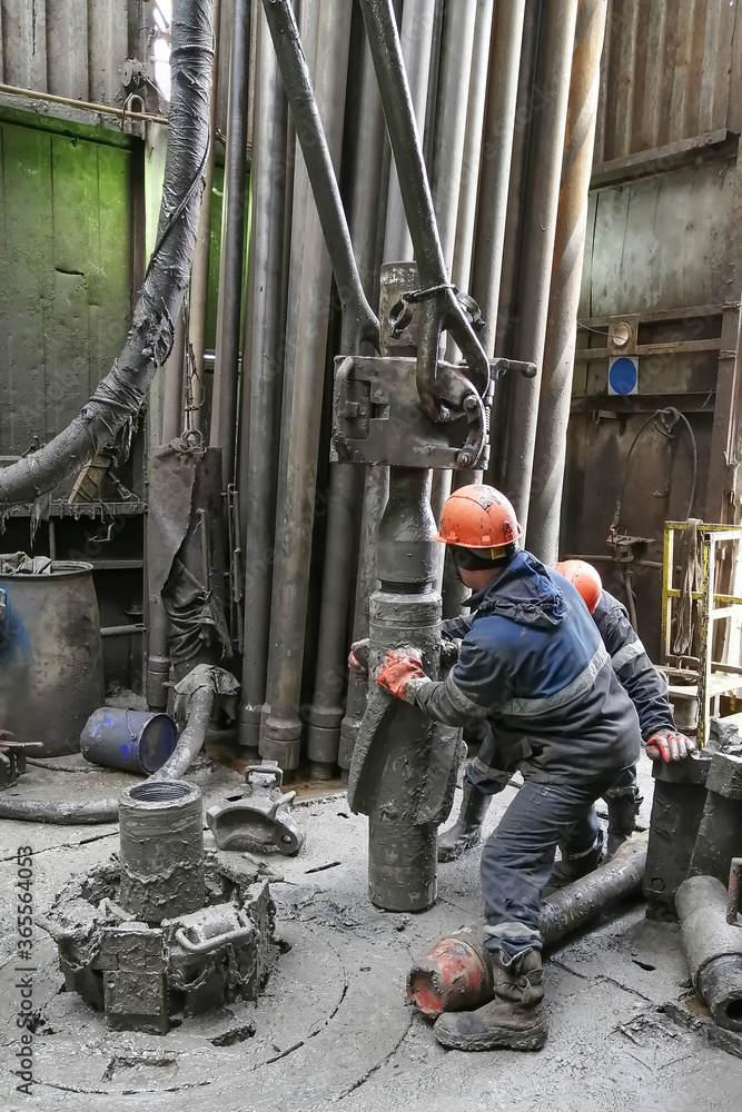 Two drilling crew workers dismantle the bottom of the drill string. Unscrewing the spiral calibrator. Working with a machine key. They are located on the rotary platform of the drilling rig. Two drilling crew workers dismantle the bottom of the drill string. Unscrewing the spiral calibrator. Working with a machine key. They are located on the rotary platform of the drilling rig.