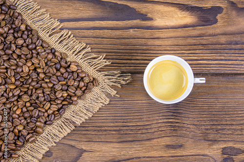 Arrow-shaped coffee beans indicate a cup of coffee. View from above. Cup of coffee and roasted coffee grains on a wooden background.