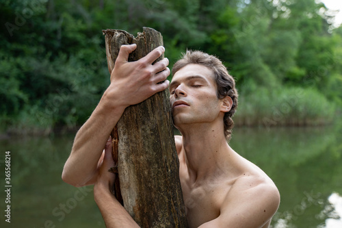 Shirtless man with eyes closed embracing wood against trees in forest