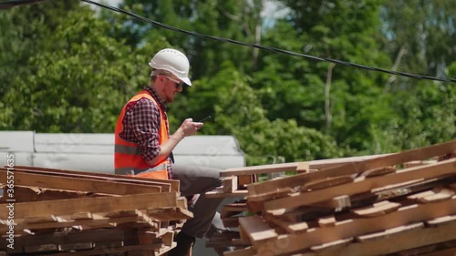 An engineer in a construction uniform talks on the phone against the background of a building under construction