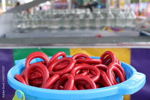 Canvastavla Closeup of red rings in blue bucket for ring toss at carnival, with clear glass bottles in bokeh effect in background