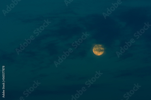 Full moon behind clouds in a blue sky. © aminkorea