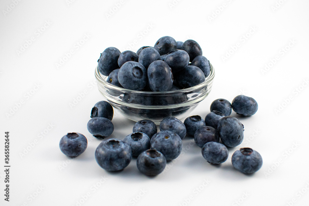 Close up photo of blueberries spilling out of a small glass bowl on a white background Close up photo of blueberries spilling out of a small glass bowl on a white background