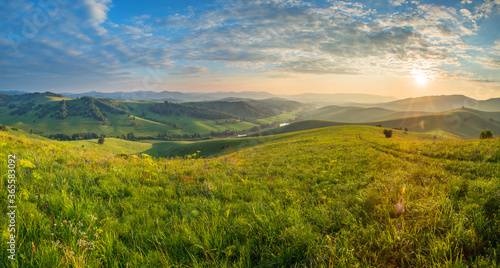 Scenic summer view. Setting sun  beautiful sky. Green hills and meadows.