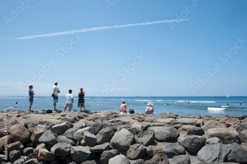 People on the rock watching surfers surfing, jetstream in the sky photo