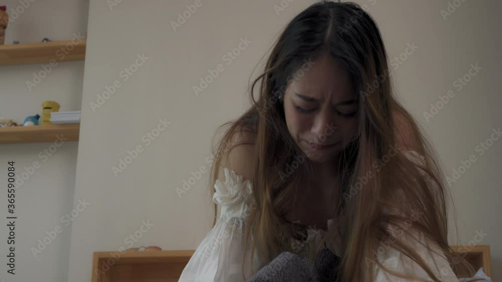 Depressed Young beautiful Asian woman sitting alone on the bed in apartment bedroom with crying and screaming. Loneliness sad girl think of grief trouble. Negative emotion and mental health concept. Depressed Young beautiful Asian woman sitting alone on the bed in apartment bedroom with crying and screaming. Loneliness sad girl think of grief trouble. Negative emotion and mental health concept.
