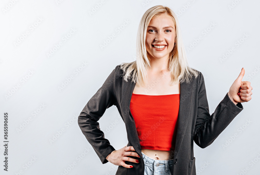 Smiling woman showing thumbs up and looking at the camera over white background. Positive girl shows like. OK
