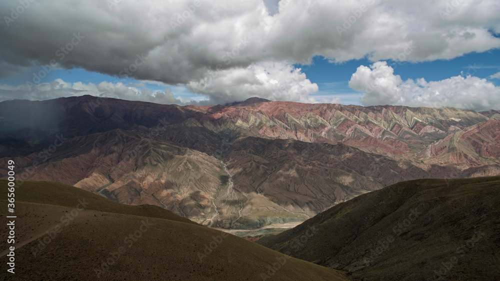 Fototapeta premium Hiking. Path across the golden meadow, valley and mountains. Aerial view of the popular landmark mountain Hornocal. Its beautiful texture and colorful rocks under a dramatic sky. 