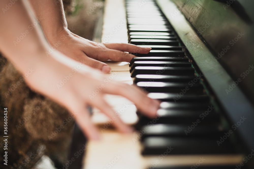 Fototapeta premium The girl plays the piano, photo in large plan. Background image of an old piano. Classic keys, music 