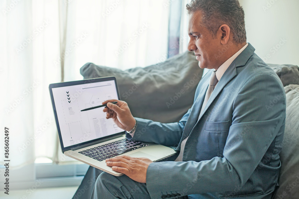 mixed race 40s buissnessman pointing at a laptop with a pen mixed race 40s buissnessman pointing at a laptop with a pen