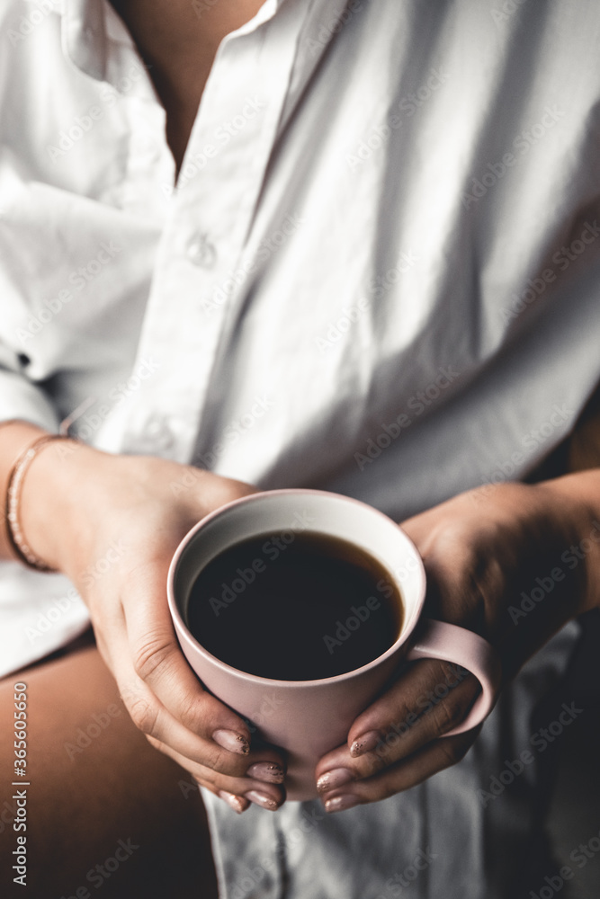 Woman in a white t-shirt holds morning coffee in a pink ceramic cup. Manicure. Front view Woman in a white t-shirt holds morning coffee in a pink ceramic cup. Manicure. Front view
