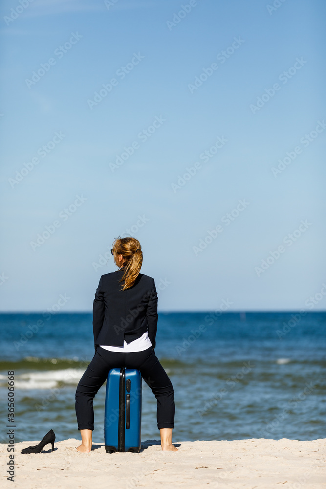 Woman with suitcase sitting on beach
