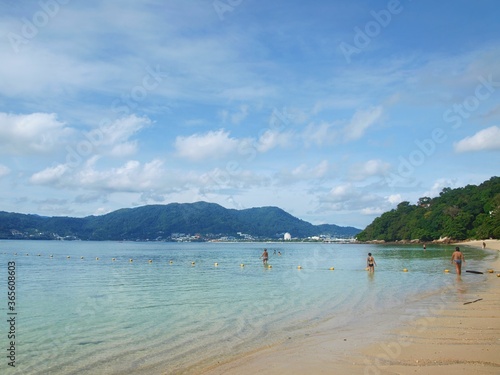 Tropical island in Thailand. People, swimming in the sea. Popular resort. Beach on Phuket. Thai paradise. Beautiful sky with cumulus clouds. Palm trees, green hills, a beautiful bay. Azure clear water