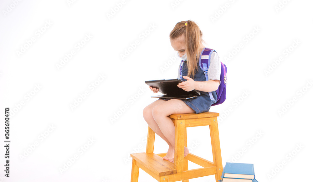 first-grader in medical mask learns to read. little girl on home distance learning. child in medical mask works at laptop and books. doing homework. isolated on white background. knowledge day first-grader in medical mask learns to read. little girl on home distance learning. child in medical mask works at laptop and books. doing homework. isolated on white background. knowledge day