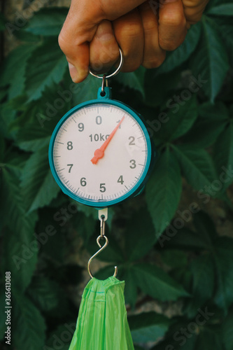 Spring scales show exactly one kilogram. A man weighs a purchase in a plastic bag. photo