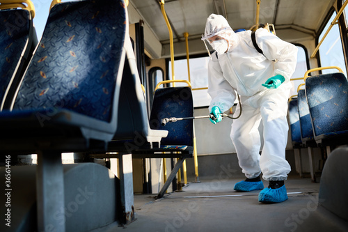 Fotografie Below view of man in protective suit doing disinfection of public bus during coronavirus pandemic