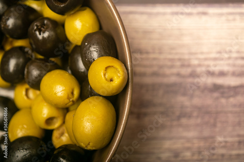 Green olives and black olives in a ceramic bowl on a wooden background. Close up.