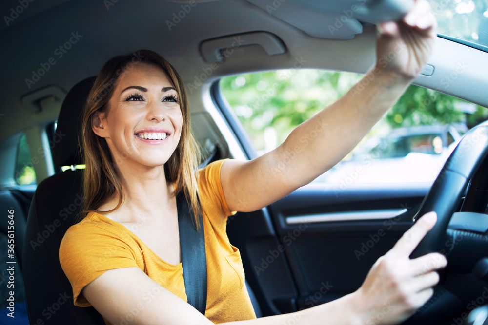 Naklejka premium Car interior view of female woman driver adjusting mirrors before driving a car. Girl enjoys driving automobile.