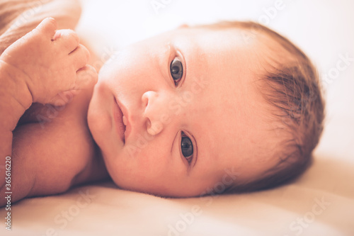 Adorable baby in white sunny bedroom in morning. Newborn child relaxing in bed. Family morning at home. Newborn kid during tummy time smiling happily at home.