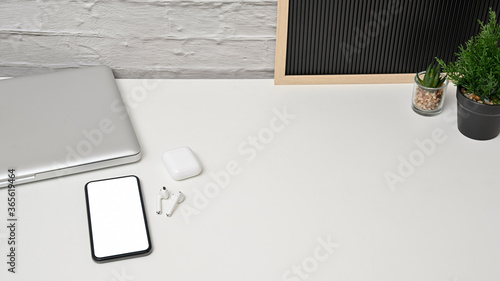 Cropped shot view of modern home office workspace with laptop blank screen smartphone and earphones on white table. concept work from home