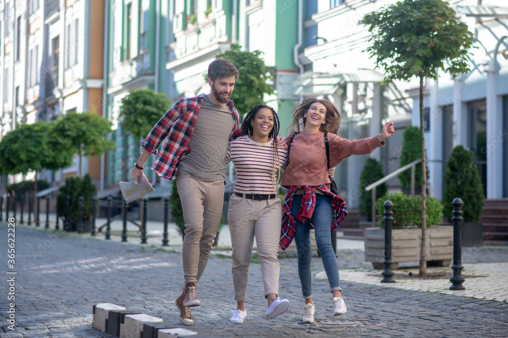 Two girls and a guy with a map bouncing up hugging