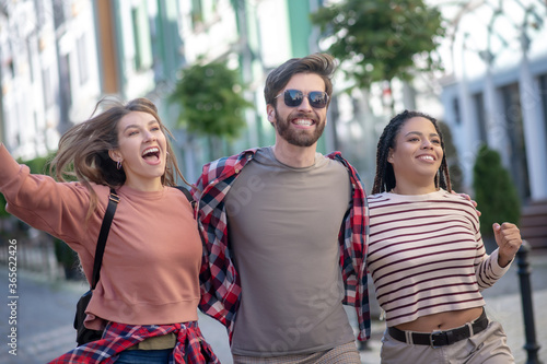 Guy in sun glasses and two pretty girls walking enthusiastic