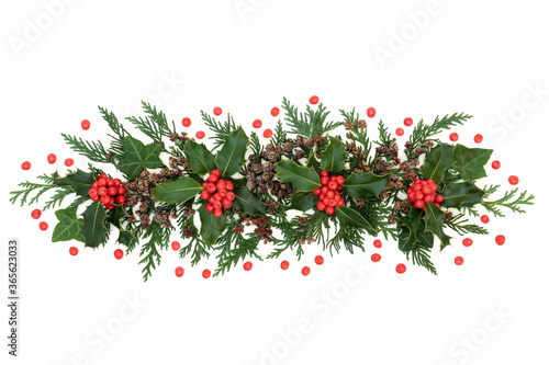Winter greenery with holly & loose red berries, cedar cypress leaves, ivy & pine cones forming a festive display element for Christmas & New Year on white background. Flat lay, top view, copy space.
