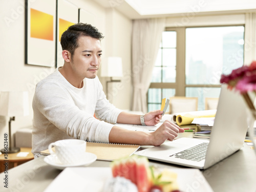 young asian man designer working from home using laptop computer contacting client