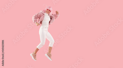 Banner of young energetic female wearing colored wig and glasses, jumping and moving as if running in air, isolated on pink background