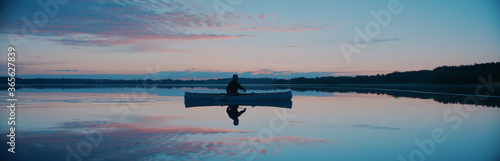 Man canoeing in a traditional wooden boat on a large lake at dawn