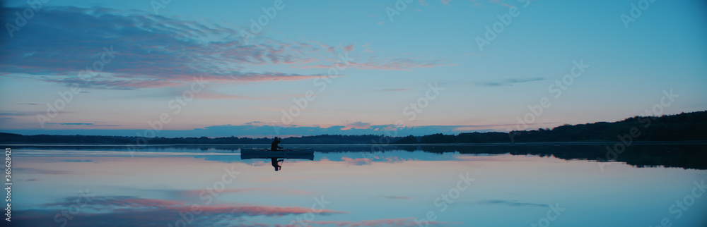 Man canoeing in a traditional wooden boat on a large lake at dawn