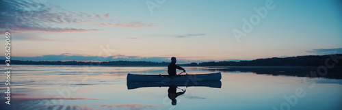 Fotografie Man canoeing in a traditional wooden boat on a large lake at dawn